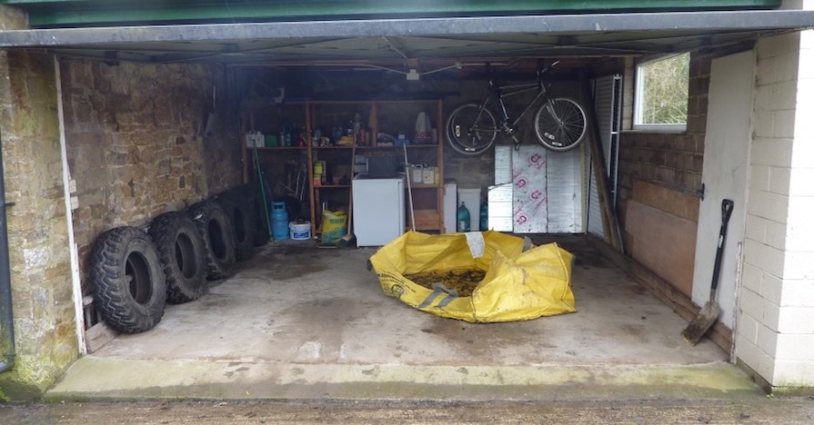 This modest, but tidy and well-organized garage has a row of tires on one wall, shelving units in the back, and a bicycle hanging from the ceiling.