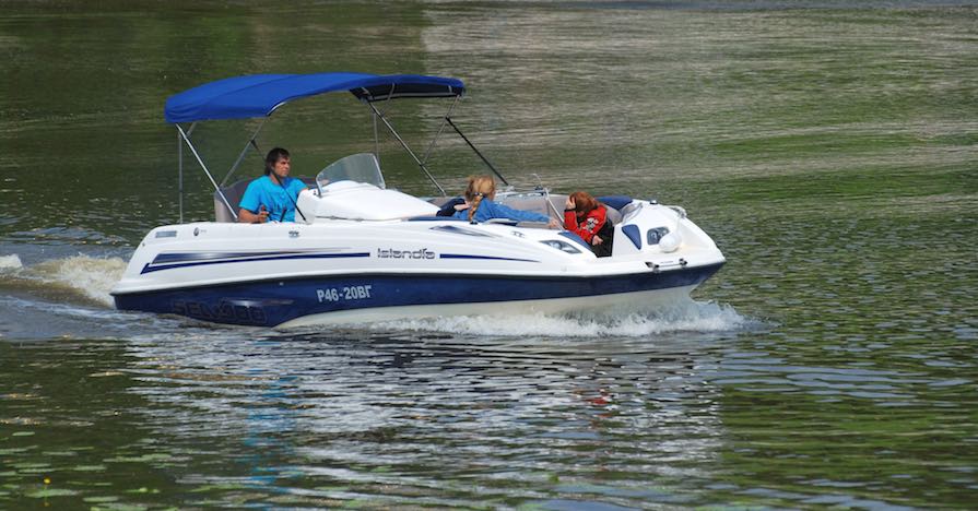 A man drives a motorboat through shimmering lake waters.